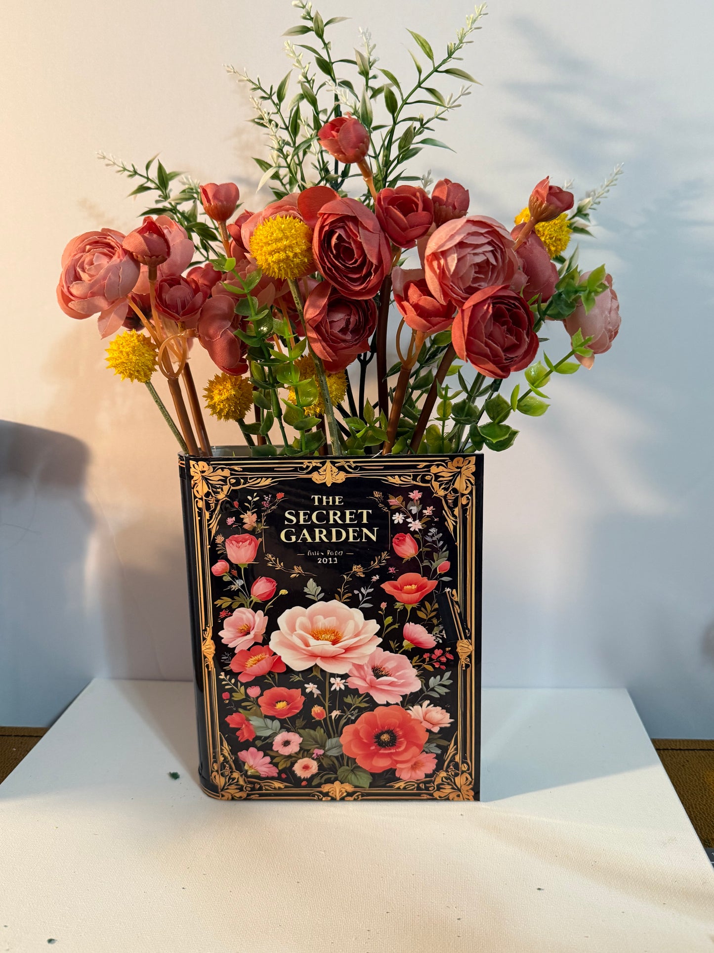 The Secret Garden decorative book vases collection with elegant gold frame detailing and black floral design, paired with artificial coral roses and yellow accent flowers