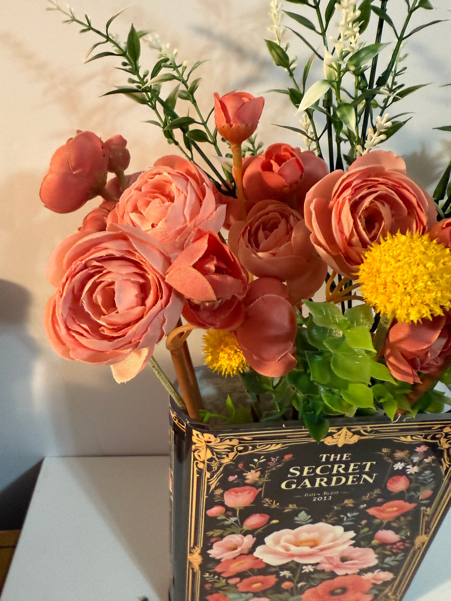 The Secret Garden decorative book vases collection with elegant gold frame detailing and black floral design, paired with artificial coral roses and yellow accent flowers
