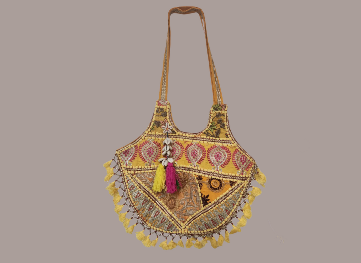 Handcrafted bohemian tote bag featuring orange base with intricate embroidery, purple and white floral patterns, shell embellishments, yellow tassels, and traditional Indian mirror work detailing