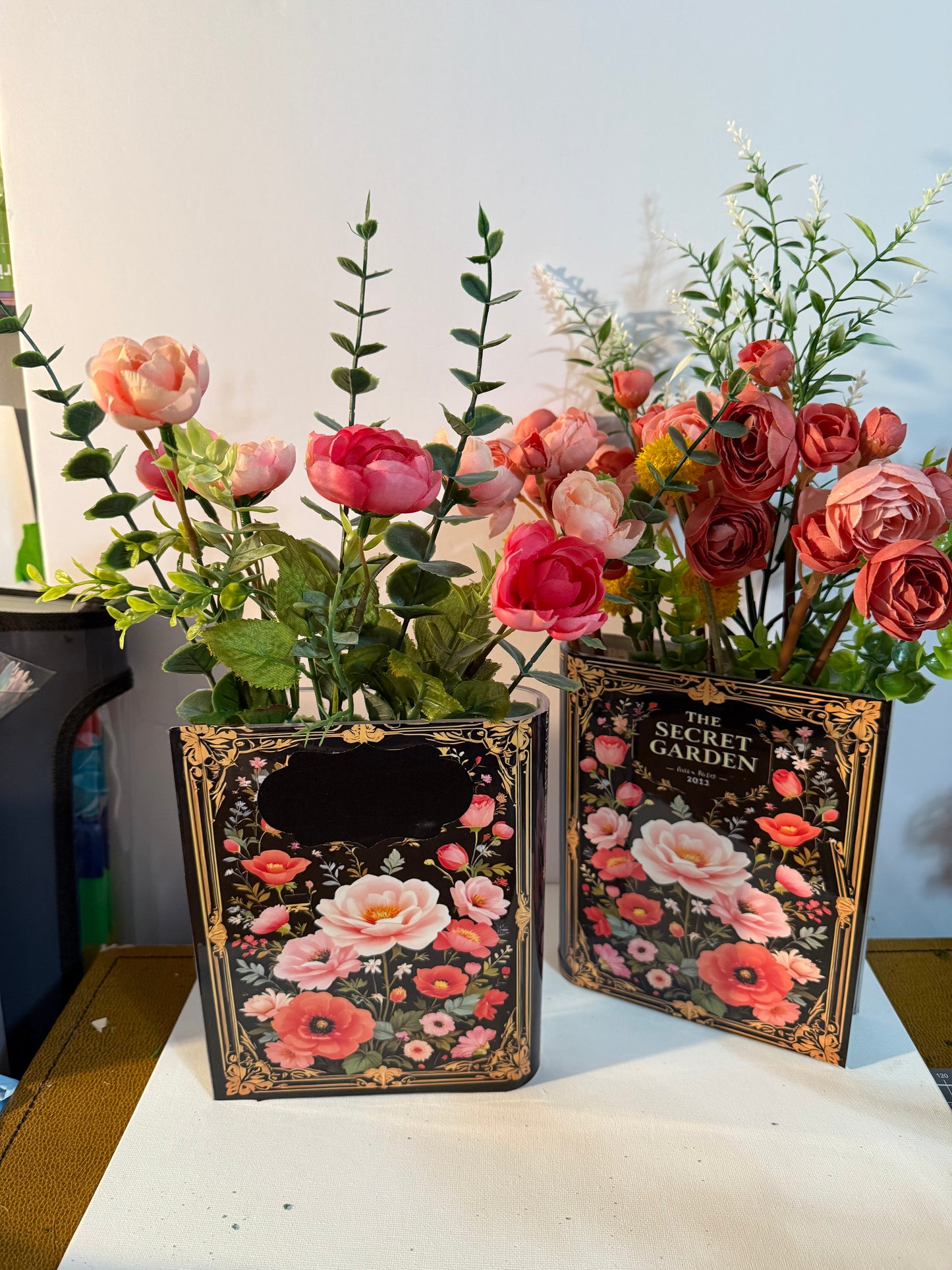The Secret Garden decorative book vases collection with elegant gold frame detailing and black floral design, paired with artificial coral roses and yellow accent flowers